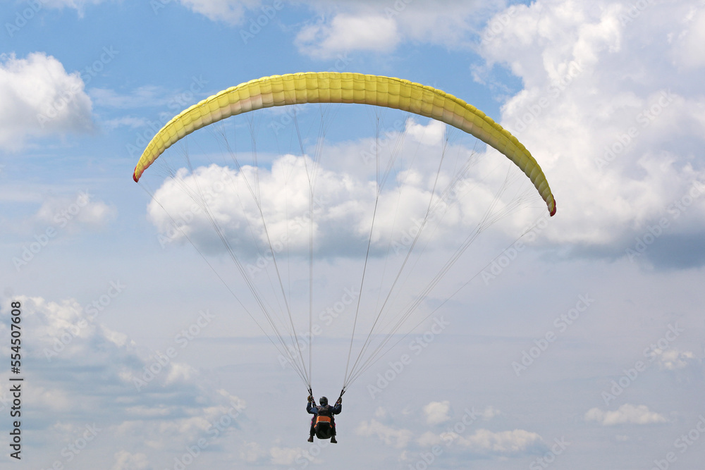 Yellow tandem Paraglider flying in a cloudy sky Yellow tandem Paraglider flying in a cloudy sky