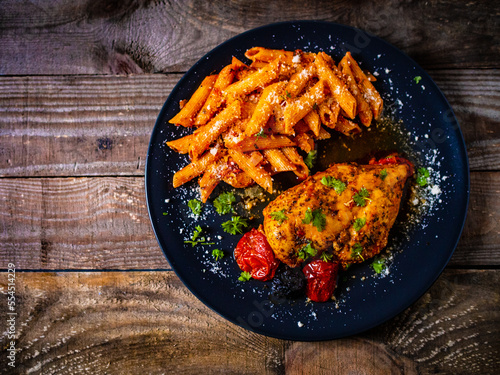 Fried chicken breast with pasta and vegetables on wooden background