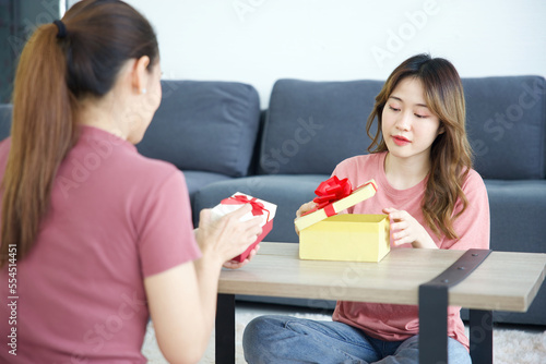 young woman smiling and opening a gift box with her friend on a table
