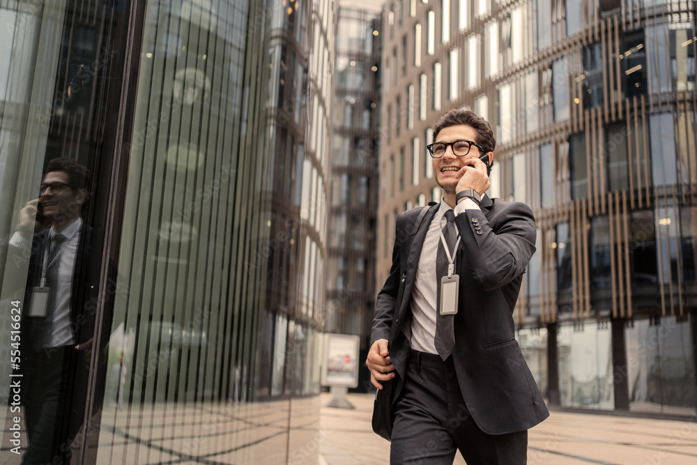 A businessman with glasses is talking on the phone, goes to work in the office in a business suit, smiles and thinks about the project.