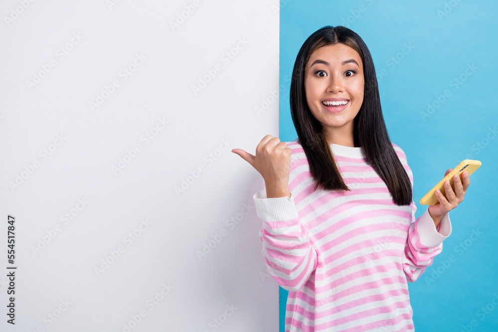 Photo of young rejoice good mood korean blogger lady hold smartphone finger point empty space new youtube channel isolated on blue color background Photo of young rejoice good mood korean blogger lady hold smartphone finger point empty space new youtube channel isolated on blue color background