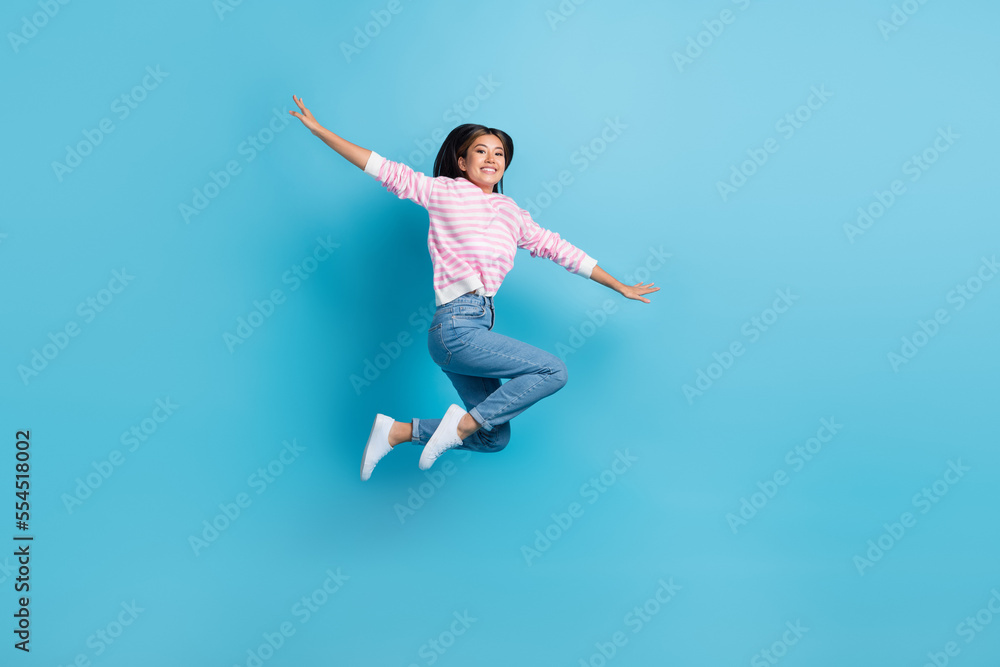 Full length photo of sweet cute girl dressed pink pullover jumping high arms sides isolated blue color background