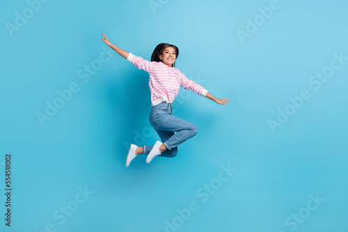 Full length photo of sweet cute girl dressed pink pullover jumping high arms sides isolated blue color background