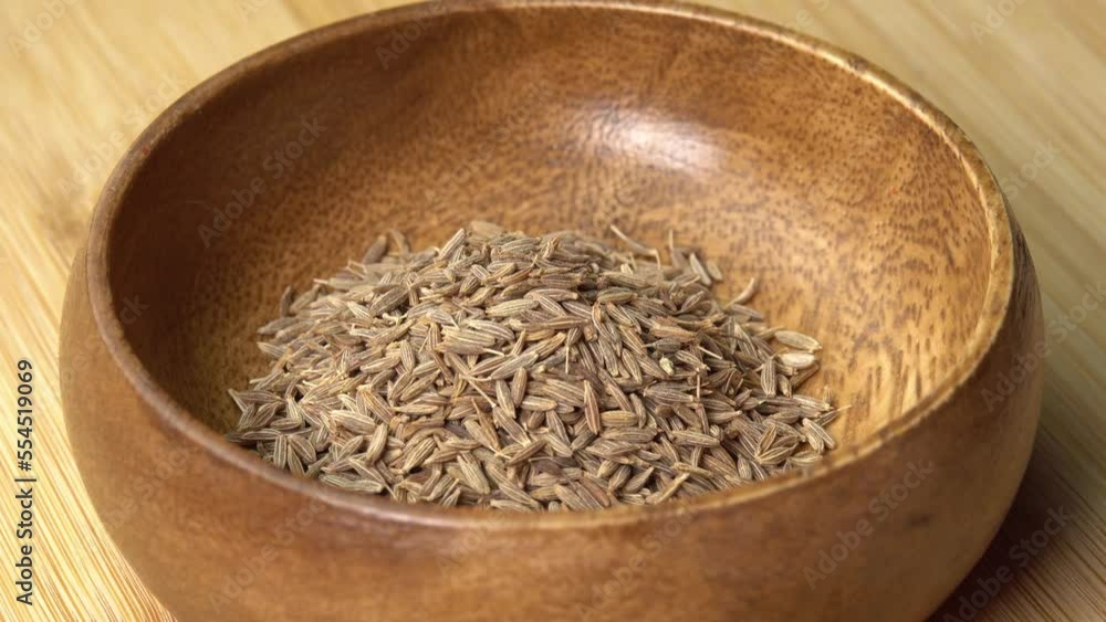 Dried cumin spice seeds lies in wooden bowl and rotating on wooden board. Dry seasoning in spoon. Spices and herbs for cooking zira Dried cumin spice seeds lies in wooden bowl and rotating on wooden board. Dry seasoning in spoon. Spices and herbs for cooking zira