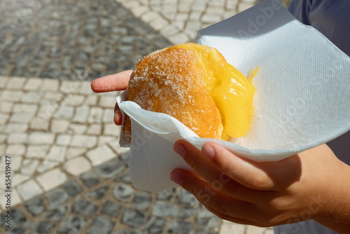 Hand holding Bola de Berlim or Berlim Ball, a Portuguese pastry made from a fried donut filled with sweet eggy cream and rolled in crunchy sugar. photo