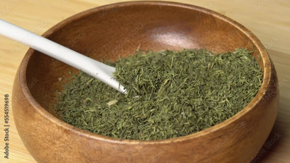 Dried dill spice in wooden bowl with spoon rotating on wooden board. Dry seasoning in spoon. Spices and herbs for cooking Dried dill spice in wooden bowl with spoon rotating on wooden board. Dry seasoning in spoon. Spices and herbs for cooking