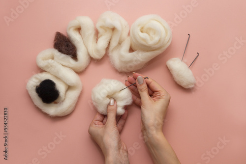 woman hand holding needle felting kit. felted woolen needle and skein of wool on pink table, flat lay