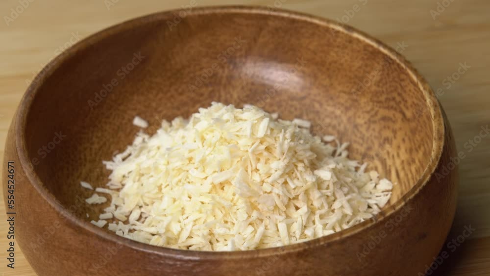 Coconut flakes lies in wooden bowl and rotating on wooden board. Coconut shavings or grated coconut rotating Coconut flakes lies in wooden bowl and rotating on wooden board. Coconut shavings or grated coconut rotating