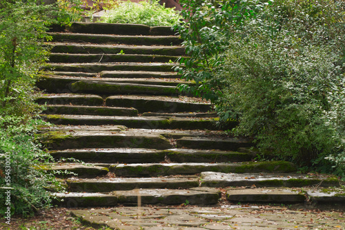 Steep stone staircase with uneven steps on the slope in the landscape design of the park. Fallen leaves are lying on the steps.