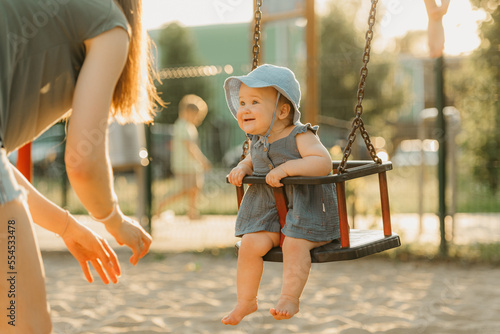 Obraz na płótnie Toddler baby girl in a dress is joying on a swing on the warm summer evening w salonie