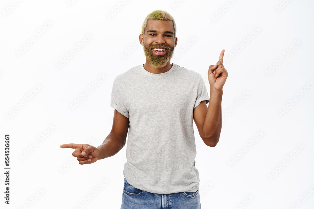 Stylish black man with yellow beard, points sideways, shows up and left promo text, empty copy space, smiles as advertises store offers, white background Stylish black man with yellow beard, points sideways, shows up and left promo text, empty copy space, smiles as advertises store offers, white background