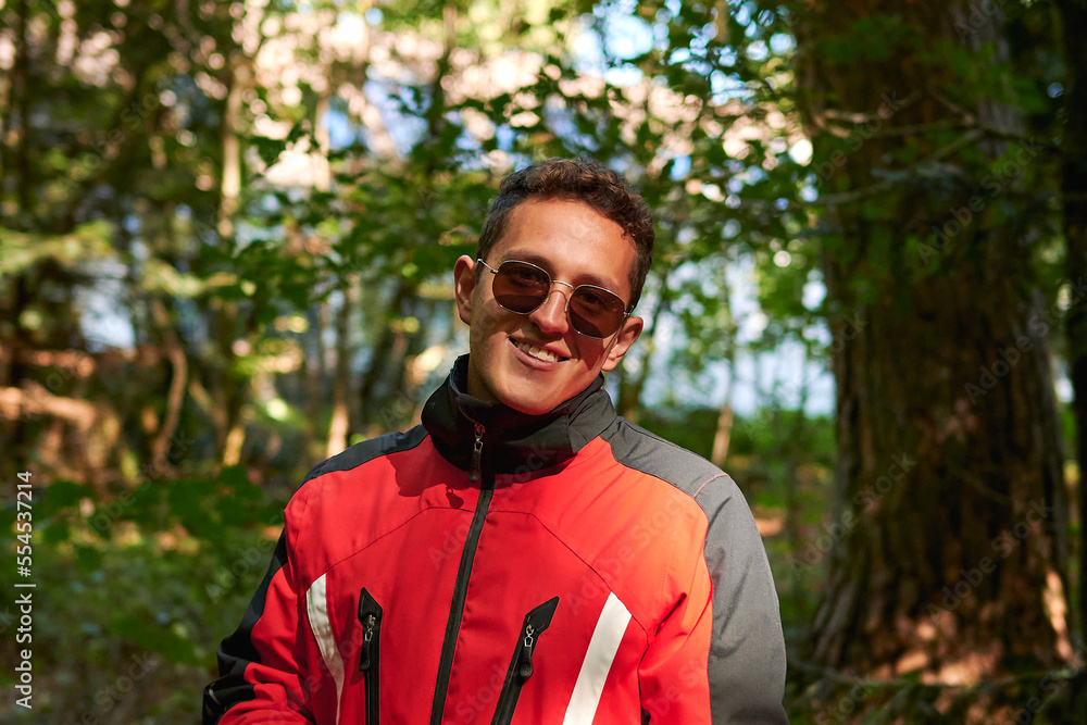 A shallow focus shot of handsome young Hispanic man with sunglasses and coat smiling in nature