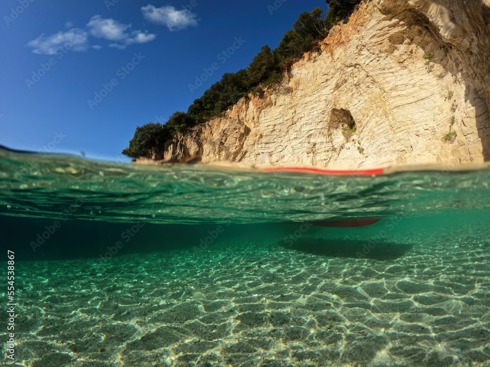 Underwater split photo of sport canoe anchored in tropical exotic island pebble beach with crystal clear turquoise sea forming a blue lagoon