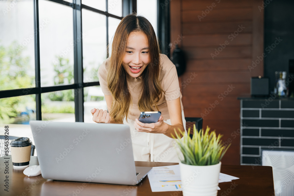 Excited female smile got good news on smartphone while working on computer at cefa, social media network, Asia young woman holding mobile smart phone raising hands celebrate with laptop, happy success Excited female smile got good news on smartphone while working on computer at cefa, social media network, Asia young woman holding mobile smart phone raising hands celebrate with laptop, happy success