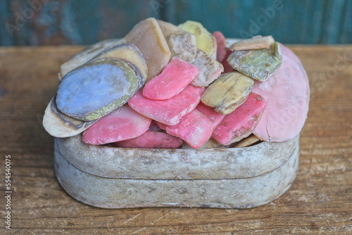 a white dirty plastic soap dish with a bunch of old colored bars of soap stands on a brown wooden table