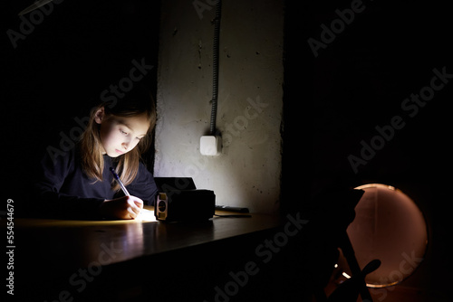 The girl learns lessons in the dark. A child does school work when there is no electricity at home.