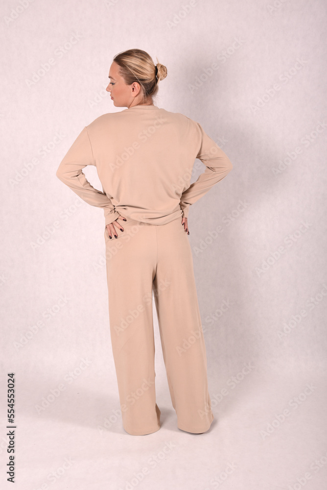© Шамиль Алиев - A young girl in beige home clothes on a white background in the studio is standing with her back