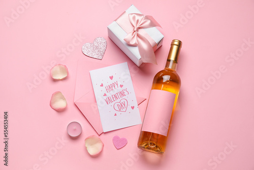 Letter with text HAPPY VALENTINE'S DAY, rose petals, gift and bottle of wine on pink background