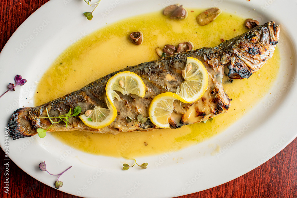 Grilled Fish. Branzino, whole grilled sea bream. Classic regional Greek  seafood favorite. Whole fish, grilled with skin in, served with lemon potatoes lemons Italian parsley and capers.