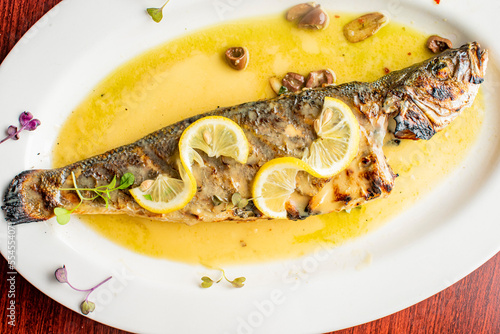 Grilled Fish. Branzino, whole grilled sea bream. Classic regional Greek  seafood favorite. Whole fish, grilled with skin in, served with lemon potatoes lemons Italian parsley and capers.