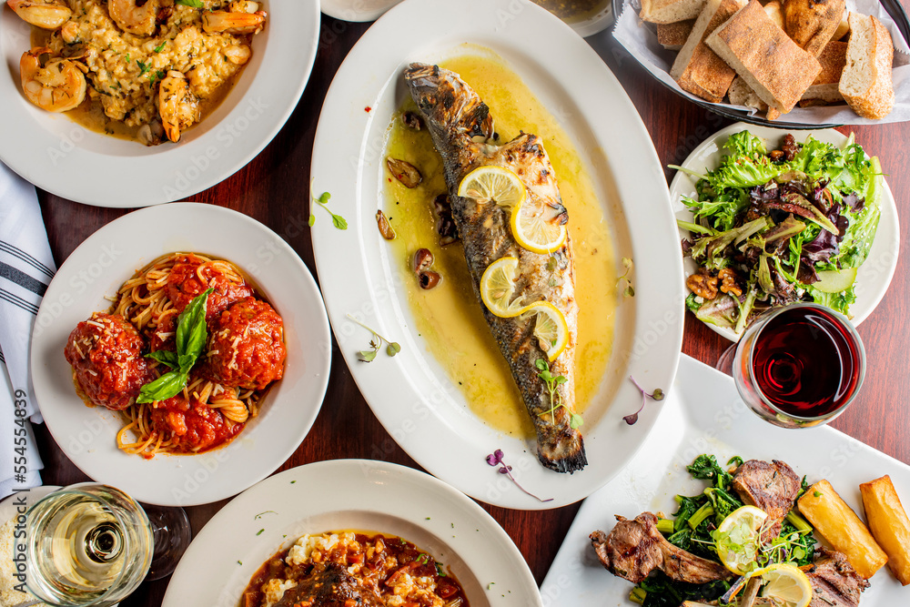 Grilled Fish. Italian Dinner table. Pasta, grilled sea bream. Classic regional Greek  seafood favorite. Whole fish, grilled with skin in, served with lemon potatoes lemons Italian parsley and capers.