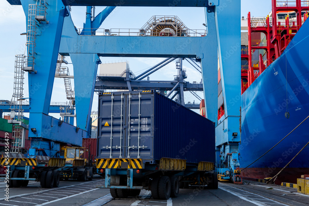 Port container terminal with a container ship in the background and a blue container in the foreground Port container terminal with a container ship in the background and a blue container in the foreground