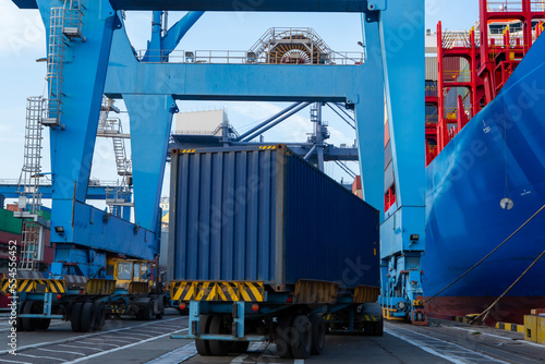 Port container terminal with a container ship in the background and a blue container in the foreground