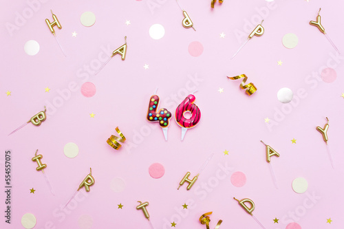 Festive candles figures in the shape of sweet donuts on a pink background surrounded by confetti. Concept of celebrating 46 years. Selective focus