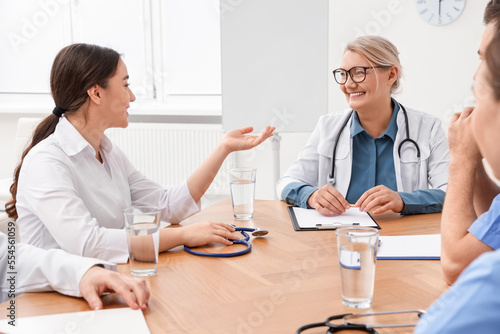 Medical conference. Doctor having discussion with speaker at wooden table in clinic