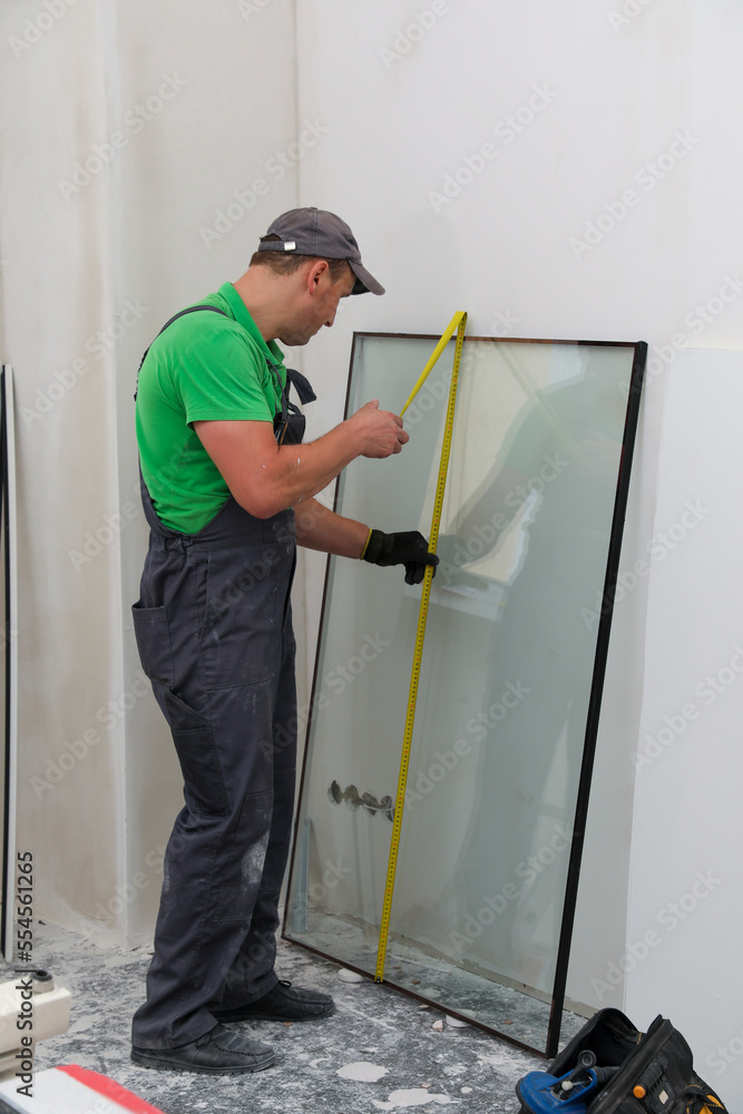 Worker in uniform measuring double glazing window indoors Worker in uniform measuring double glazing window indoors