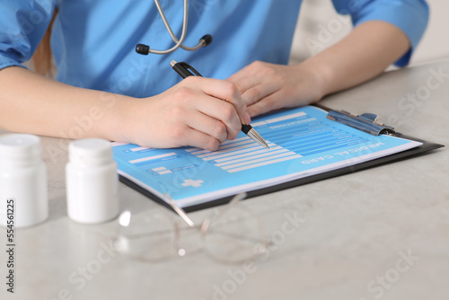 Doctor filling patient s medical card at table in clinic  closeup