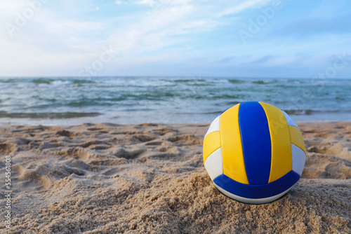 Colorful volleyball ball on sand near sea. Space for text
