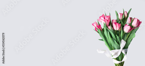 Pink tulips bouquet tied with white satin ribbon on gray background