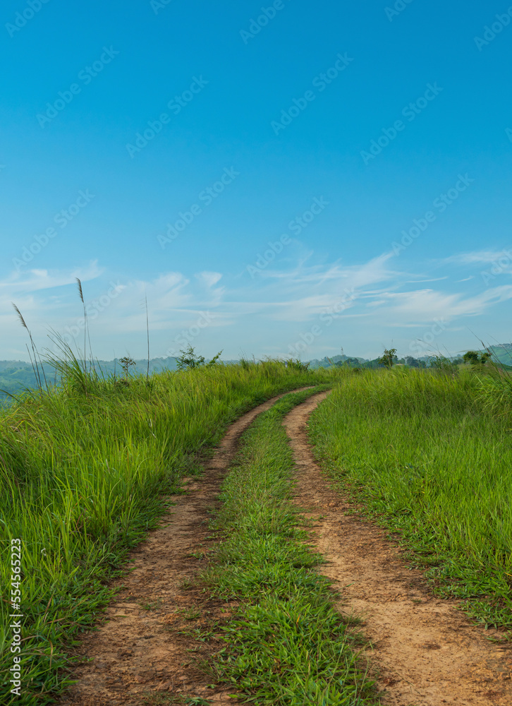 Landscape view of countryside dirt road path crosses the hills with blue sky background.