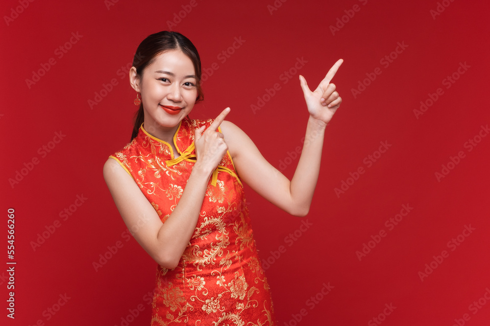Young asian woman wearing qipao cheongsam dress with hand point to copy space on red background for Chinese new year festival Young asian woman wearing qipao cheongsam dress with hand point to copy space on red background for Chinese new year festival