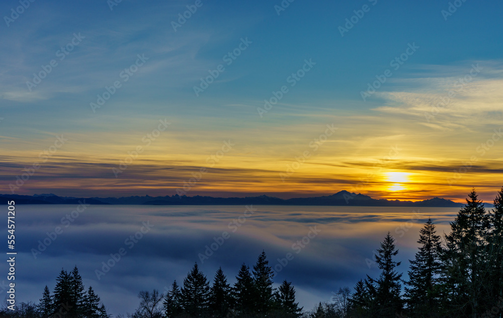 Dense cloud inversion over Fraser Valley, BC,  as seen from a University Highlands residence, with starburst sunrise over distant alpine mountains in silhouette.