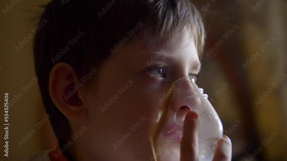 a sad child is treated by breathing in a mask with inhalations. treatment of allergy cough by inhalation. boy at home breathing in a mask with an inhaler a sad child is treated by breathing in a mask with inhalations. treatment of allergy cough by inhalation. boy at home breathing in a mask with an inhaler