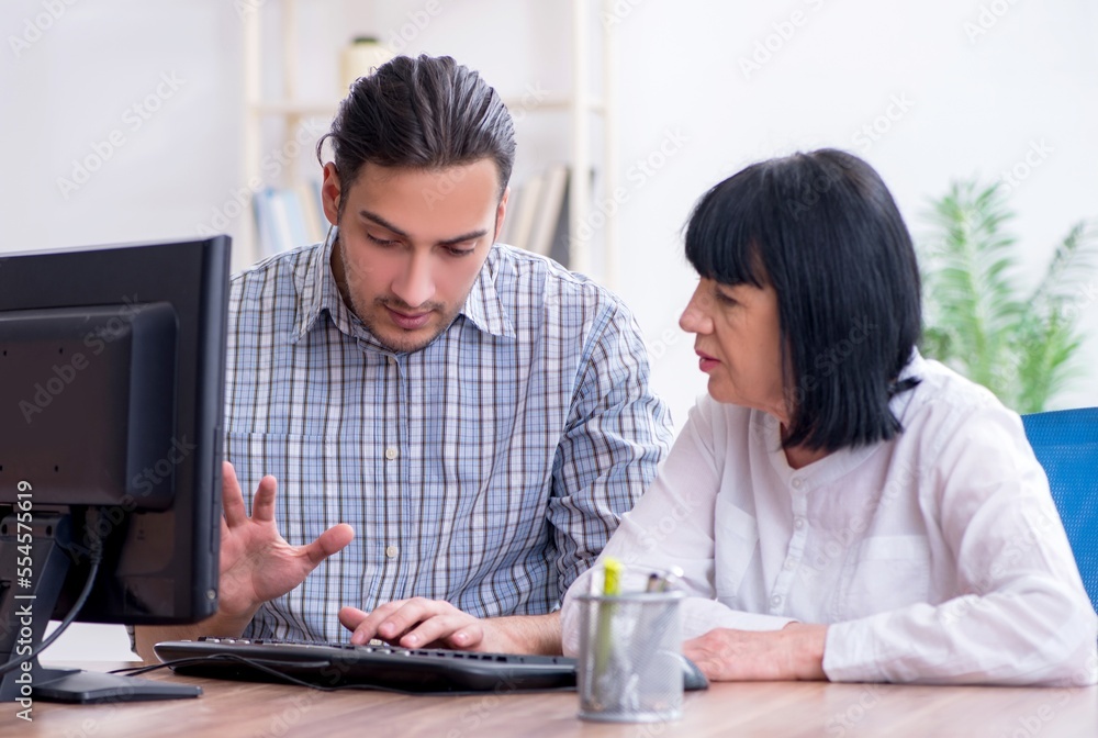 Young male employee explaining to old female colleague how to us Young male employee explaining to old female colleague how to us
