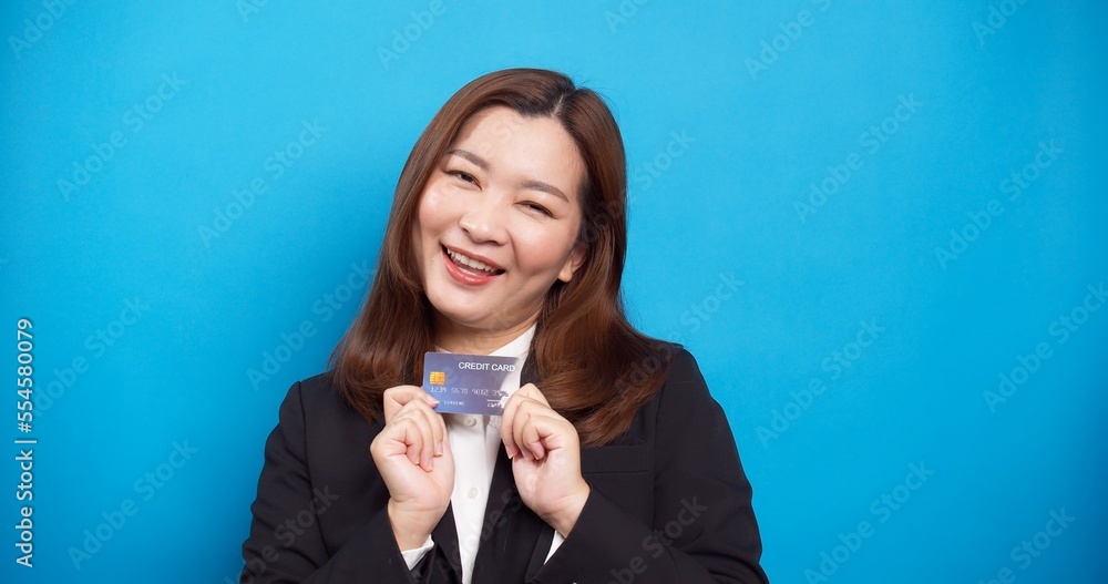 Beautiful Asian businesswoman in black suit holding credit card with a smile in the studio shot on blue background Beautiful Asian businesswoman in black suit holding credit card with a smile in the studio shot on blue background