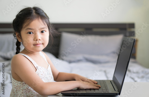 Asian child student or kid girl learning study online or learn from home on computer notebook or play laptop by kindergarten studying to primary education and happy smile on back to school in bedroom