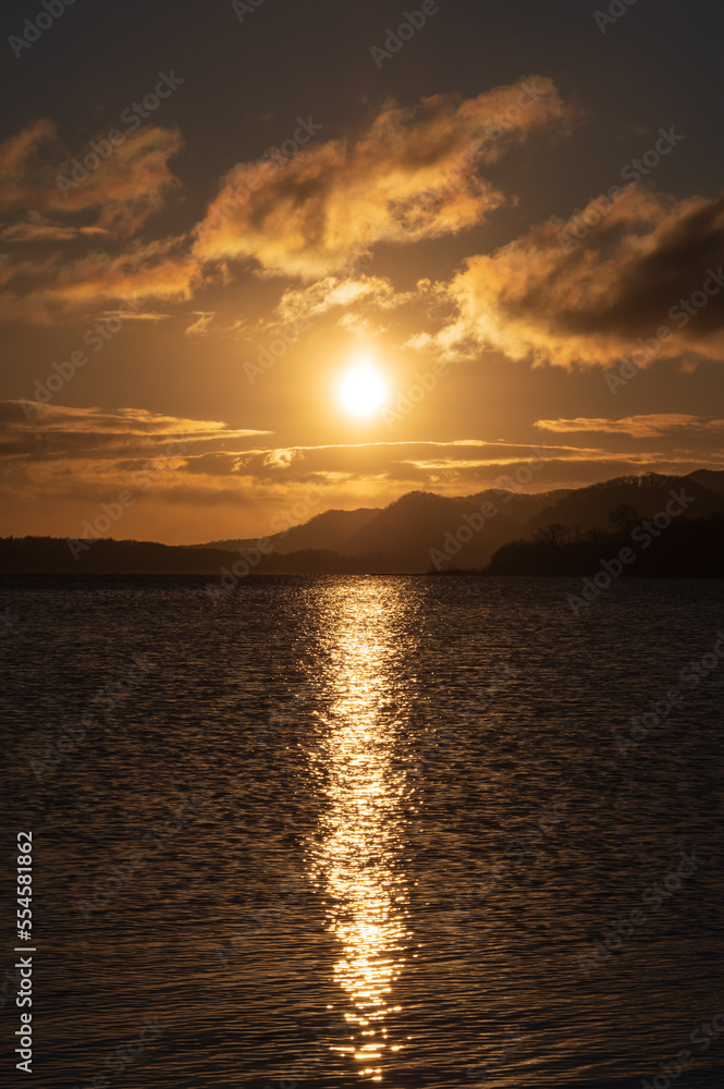 湖上の空に眩しく光る太陽の光がさざ波の湖面に反射する。薄い黄金色の暗めの雰囲気。