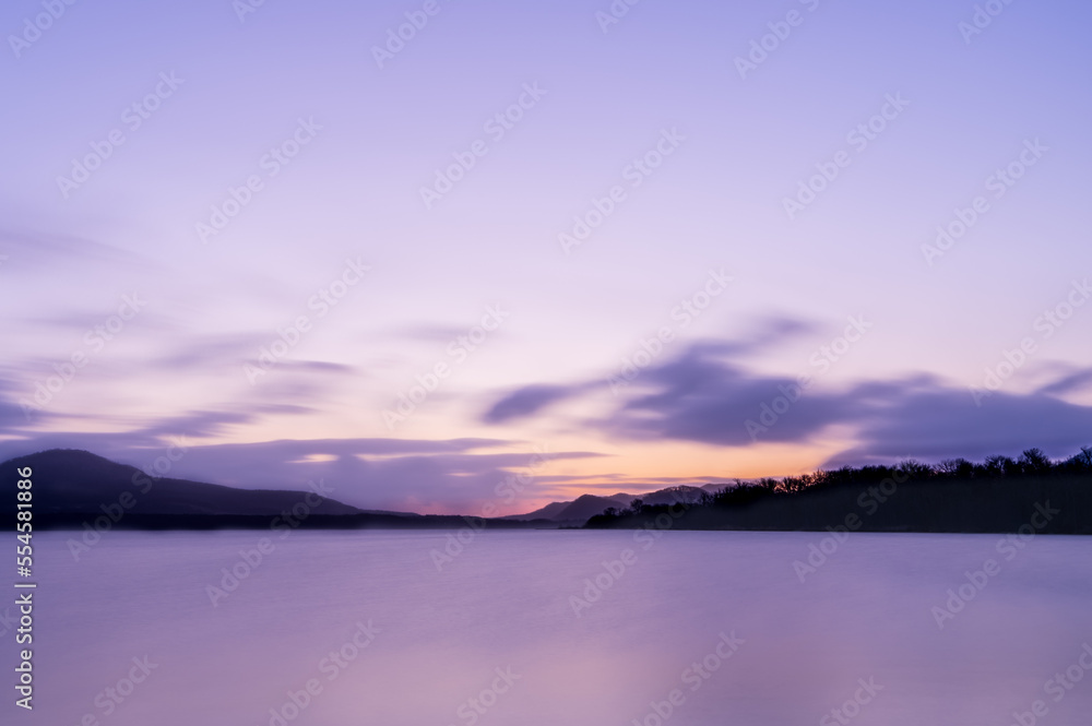 薄い紫色の夜明けの空の色を水面に反射する湖。