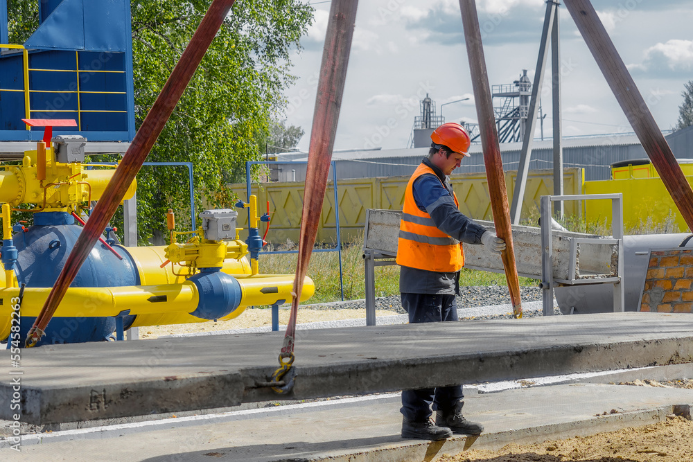 Slinger lays concrete slab on construction site on summer day. Worker
