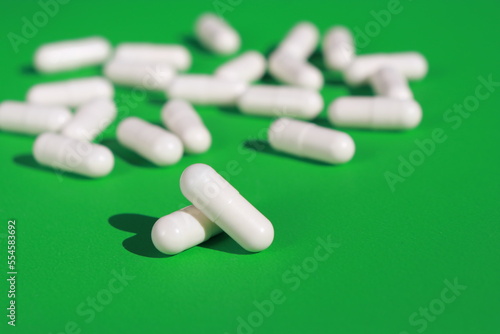 close up of white pills capsules on green background