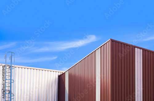 Corrugated steel wall of 2 warehouse buildings with metal stair against blue sky background in low angle view © Prapat