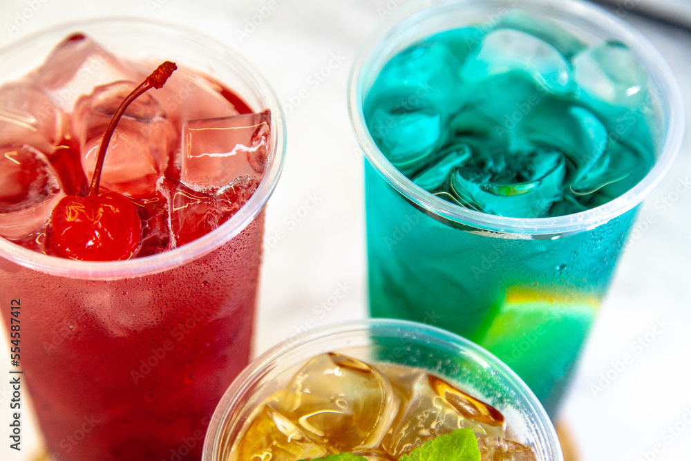 Three juicy lemonades of different colors in transparent plastic glasses with ice Three juicy lemonades of different colors in transparent plastic glasses with ice