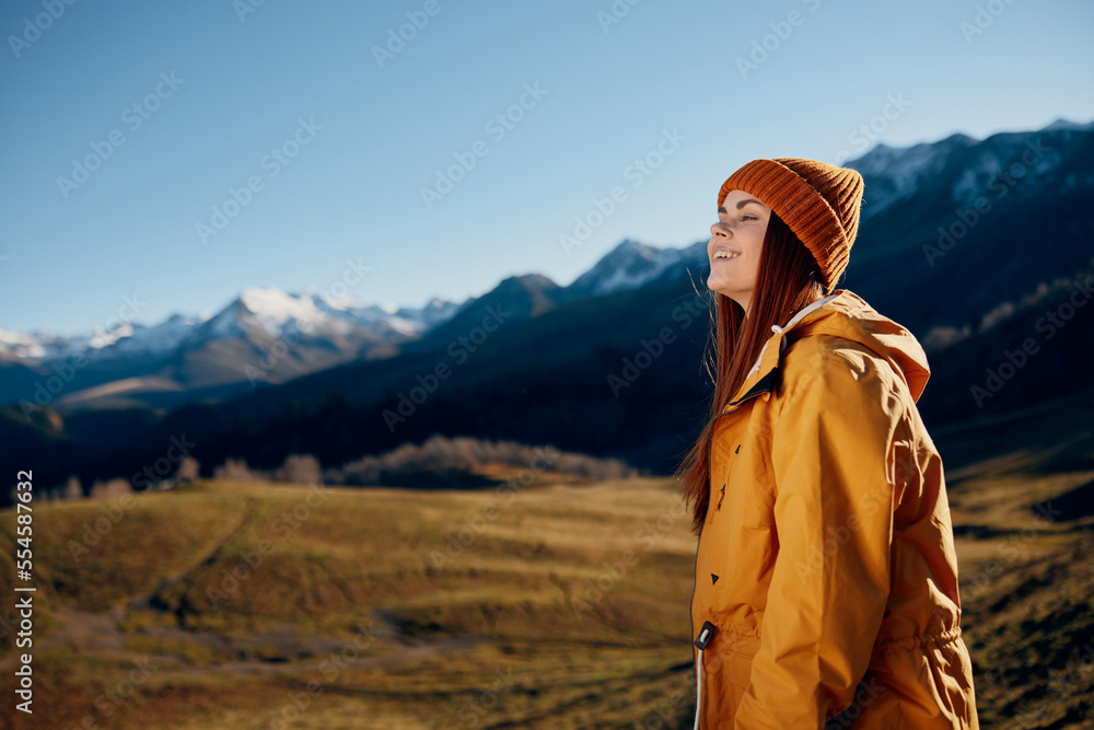 Woman standing beautifully on a hill smile with teeth in the mountains in the autumn in a yellow raincoat and jeans happy sunset trip to hike the mountains in the snow, freedom lifestyle 
