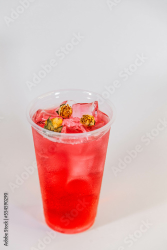 Red lemonade with ice and yellow rose buds on a white background.