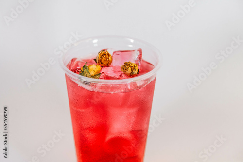 Red lemonade with ice and yellow rose buds on a white background.