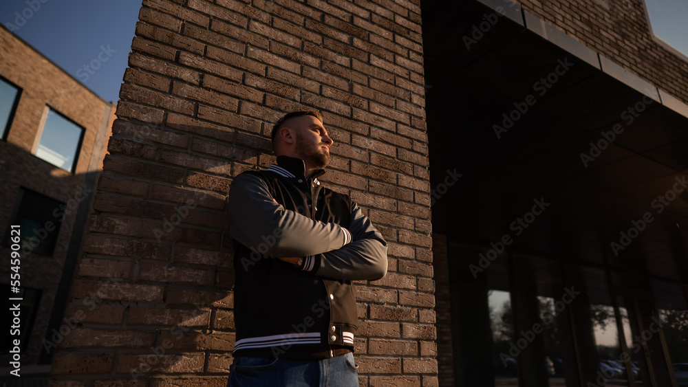 Fototapeta premium Caucasian bearded man in a bomber jacket leaned against a brick wall. 